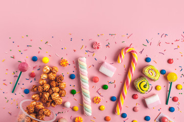 Colored, children's, unhealthy candy, marmalade, marshmallow, caramel popcorn, chupa-chups on a pink background. A table full of sweets. Top view