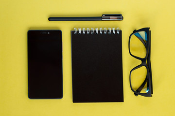 Top view on notebook, smartphone, pen and glasses on yellow background. Flat lay composition.