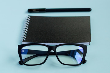 Notebook with pen and and glasses on a blue background.