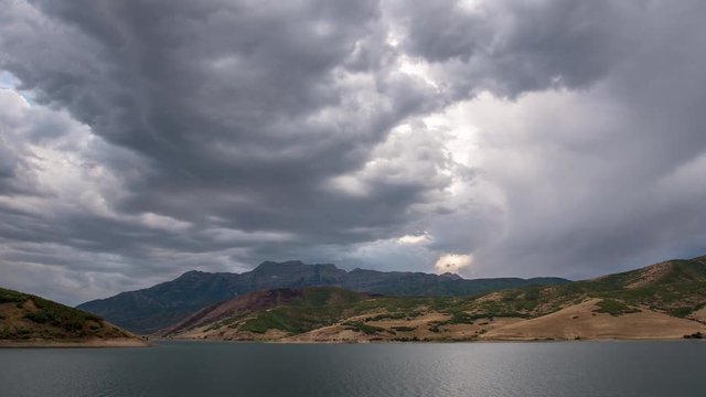 Time lapse of dark clouds moving over lake viewing mountain range at sunset.