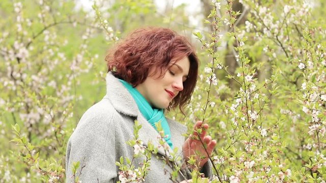 Pretty romantic young red head woman with cherry branches blossom in spring park. Spring trees background. Portrait close up.