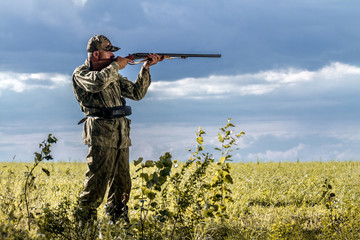 Hunting for wild animals. Hunter with a gun on the field on a cloudy sky background