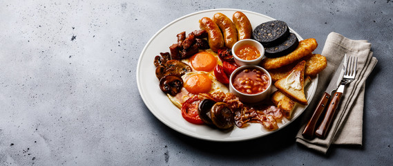 Full fry up English breakfast with fried eggs, sausages, bacon, black pudding, beans and toasts on gray concrete background