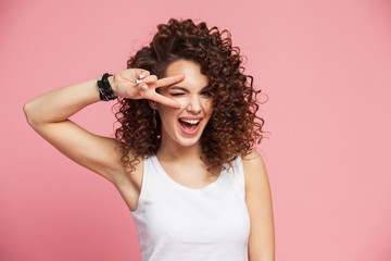 Image of happy young woman standing isolated over pink background showing peace gesture. Looking...