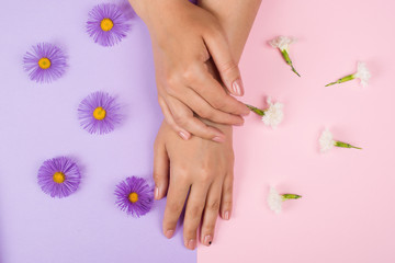 Female manicure background. Hand and nail care. Beautiful young woman's hands on pink and purple background with flowers. Hand with pastel nails. Stylish trendy women manicure.