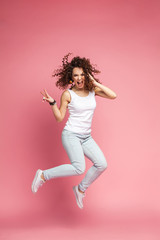 Full length portrait of a joyful young woman jumping and celebrating over pink background.