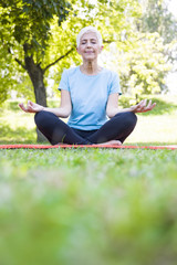 Senior woman in lotus pose sitting on green grass