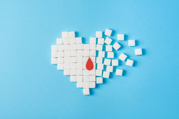 a drop of blood on broken heart made of pure white cubes of sugar isolated on blue background,...