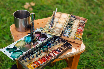 Palette of watercolor paints and brushes on the wooden background.