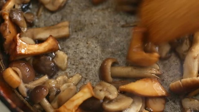 Close-up of preparation and frying of edible wild mushrooms. Mix of chanterelle, portobello, shiitake in Cast-iron pan. Cooking with spices, butter, parsley, onion, leek, garlic.