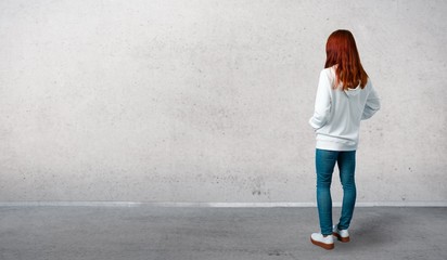 Young redhead girl in an urban white sweatshirt with glasses looking back and standing on a vintage...