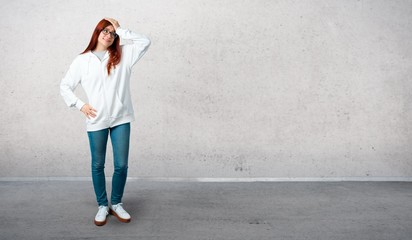 Young redhead girl in an urban white sweatshirt with glasses has just realized something and has intending the solution and standing on a vintage gray wall