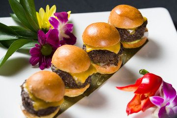 Row of four cheese burger sliders on white plate