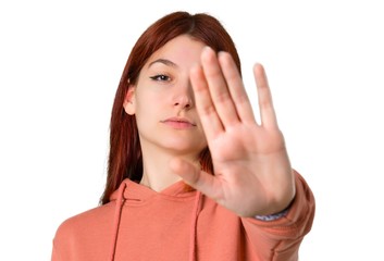 Young redhead girl with pink sweatshirt making stop gesture with her hand denying a situation that thinks wrong on isolated white background