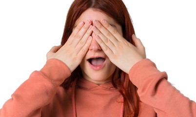Young redhead girl with pink sweatshirt covering eyes by hands. Surprised to see what is ahead on...