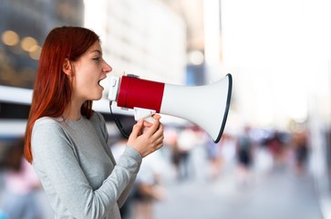 Young redhead girl shouting through a megaphone to announce something in lateral position on...