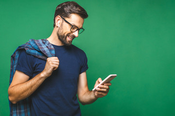 Always in touch. Smiling young man holding smart phone and looking at it. Portrait of a happy man using mobile phone isolated over green background.