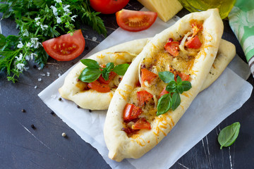 Delicious homemade Greek oval pizza with salami, tomato, onion and cheese on a dark stone background. Copy space.