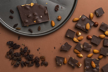 Dark chocolate pieces with roasted almonds and raisins scattered around