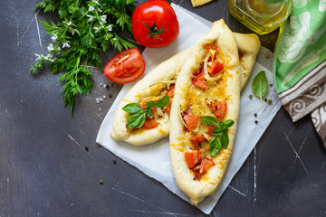 Delicious homemade Greek oval pizza with salami, tomato, onion and cheese on a dark stone background. Top view flat lay background.