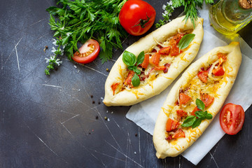 Delicious homemade Greek oval pizza with salami, tomato, onion and cheese on a dark stone background. Copy space.