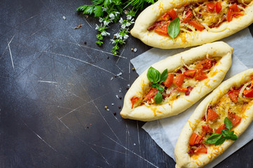Delicious homemade Greek oval pizza with salami, tomato, onion and cheese on a dark stone background. Copy space.