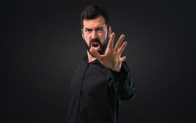 Handsome man with beard making stop sign on black background