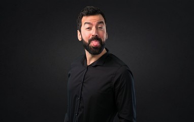 Handsome man with beard taking out his tongue on black background