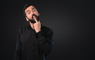 Handsome man with beard making horn gesture on black background