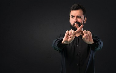 Handsome man with beard making NO gesture on black background