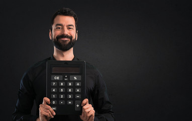 Handsome man with beard holding a calculator on black background