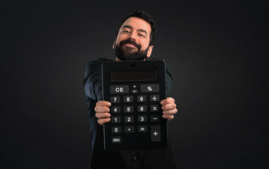 Handsome man with beard holding a calculator on black background