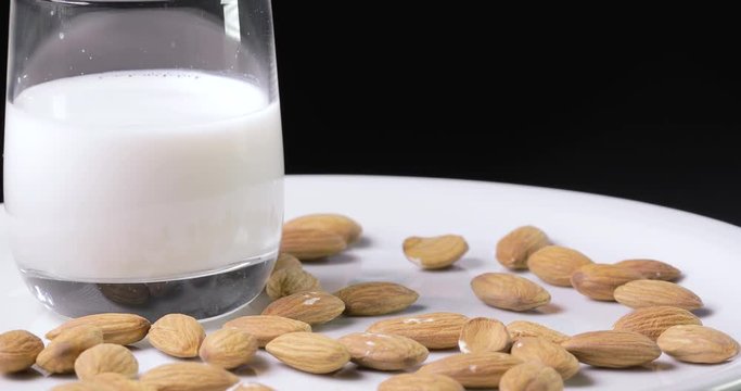 Latte di mandorla in un bicchiere disposto su un piatto bianco rotante con mandorle 