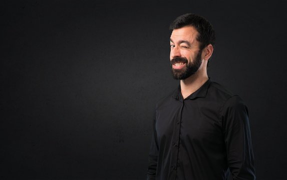 Handsome man with beard winking on black background
