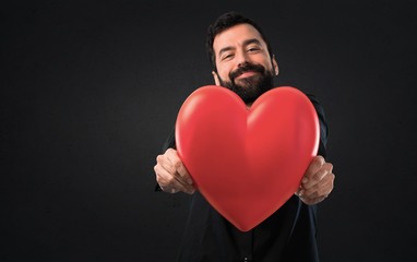 Handsome man with beard holding a heart toy on black background