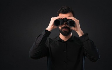 Handsome man with beard with binoculars on black background