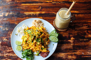 Healthy Vegetarian vegan menu Pad Thai, stir-fried rice noodles, is one of Thailand's national main dish and banana smoothies on wooden table.top view © tatyanasuyarova