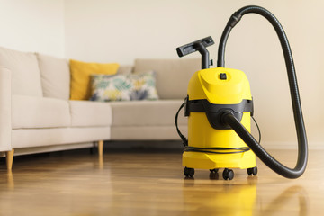 Yellow modern vacuum cleaner in living room. Copy space. Flat clean vacuuming concept - obrazy, fototapety, plakaty