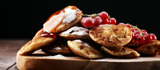 Pancakes or puffertjes with berries and maple syrup on rustic table