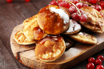 Pancakes or puffertjes with berries and maple syrup on rustic table