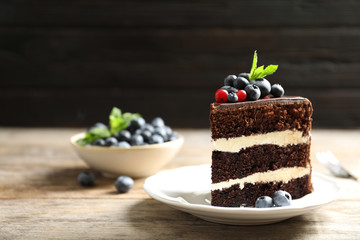 Plate with slice of chocolate sponge berry cake on wooden table