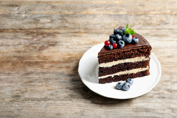 Plate with slice of chocolate sponge berry cake on wooden background