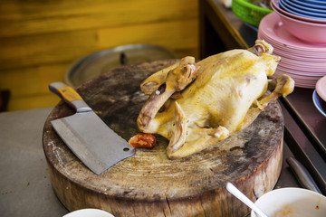 Boiled chicken, located on the chopping board is to be cut to break away for some rice and sauce, steamed chicken and white rice