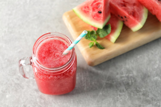 Tasty summer watermelon drink in mason jar and board with sliced fruit on table