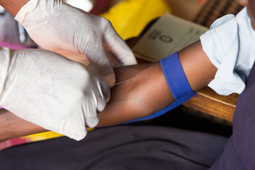 a health worker taking a blood sample from the cubital vein by piercing the vein (venipunture) and...