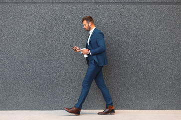 Businessman looking at his mobile phone while walking on street to office.
