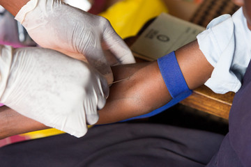 Obraz premium a health worker taking a blood sample from the cubital vein by piercing the vein (venipunture) and collecting blood into a test tube under negative pressure (vacuum). Photo taken in Uganda in 2017.