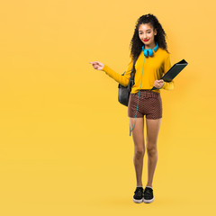 Full body of Teenager student girl with curly hair pointing finger to the side and presenting a product on yellow background