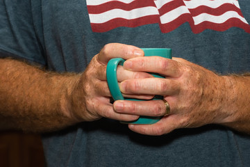 Fototapeta premium Senior male hands with age spots holding morning coffee in two hands 