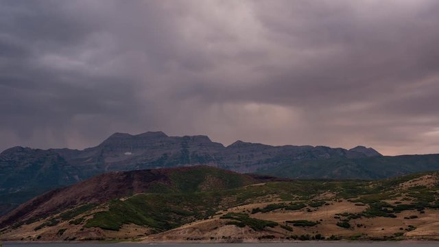 Time lapse of dark clouds moving over mountain range as they light up from the sun setting.